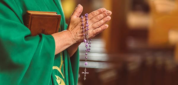 priest praying with a set of rosary beads