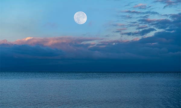 moon in a cloudy sky over the ocean