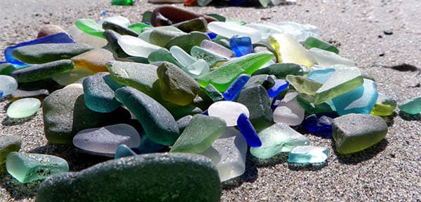 a pile of different colored sea glass on the sand